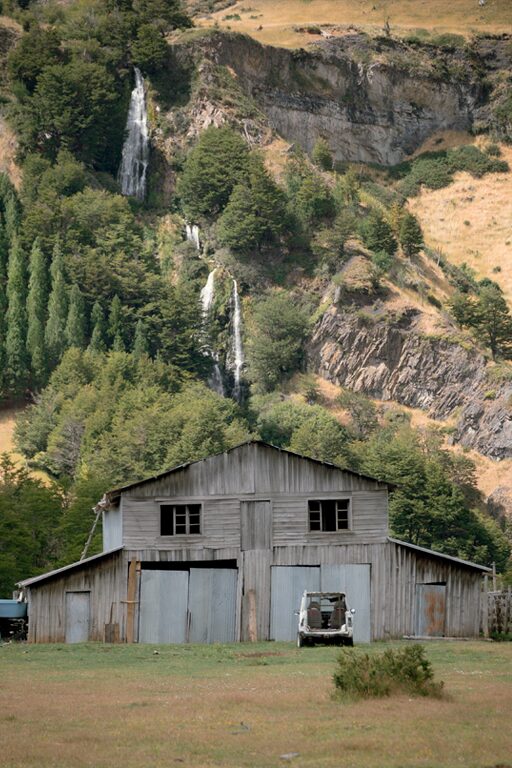 A rustic barn with a backdrop of waterfalls breaking through the forested hillside