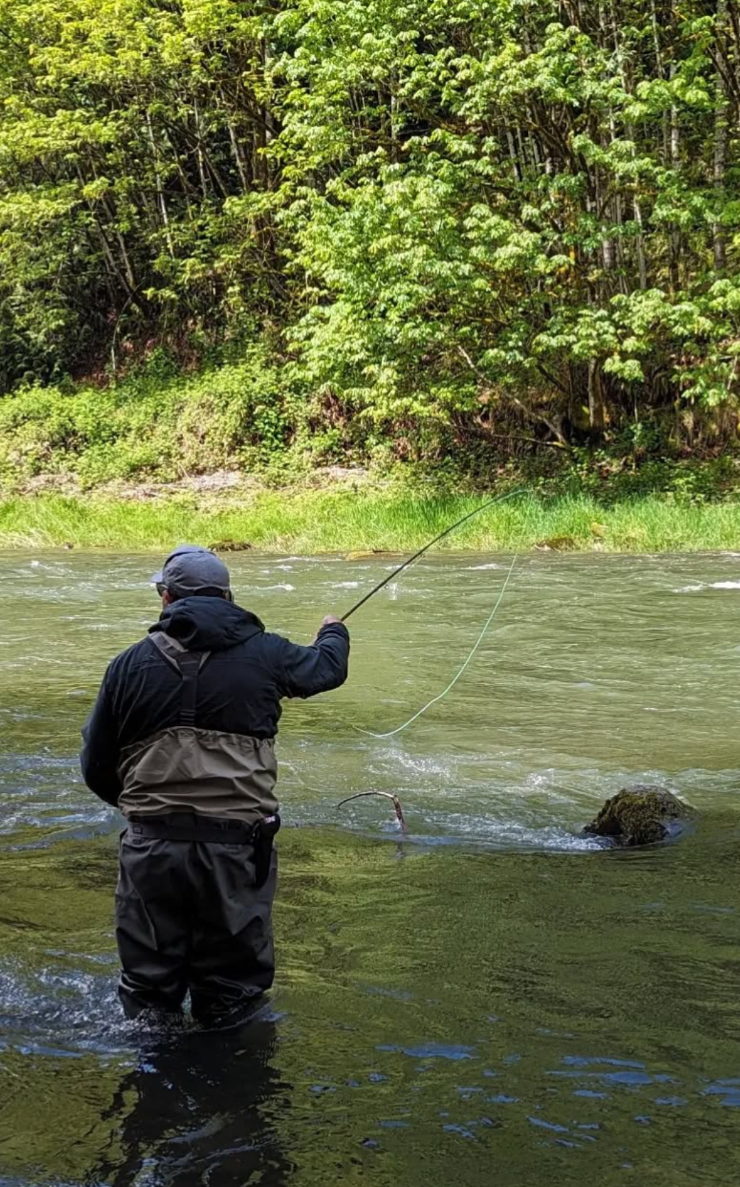 Two men fly fishing in shallow, turquoise blue water with mountain backdrop and cloudy blue sky