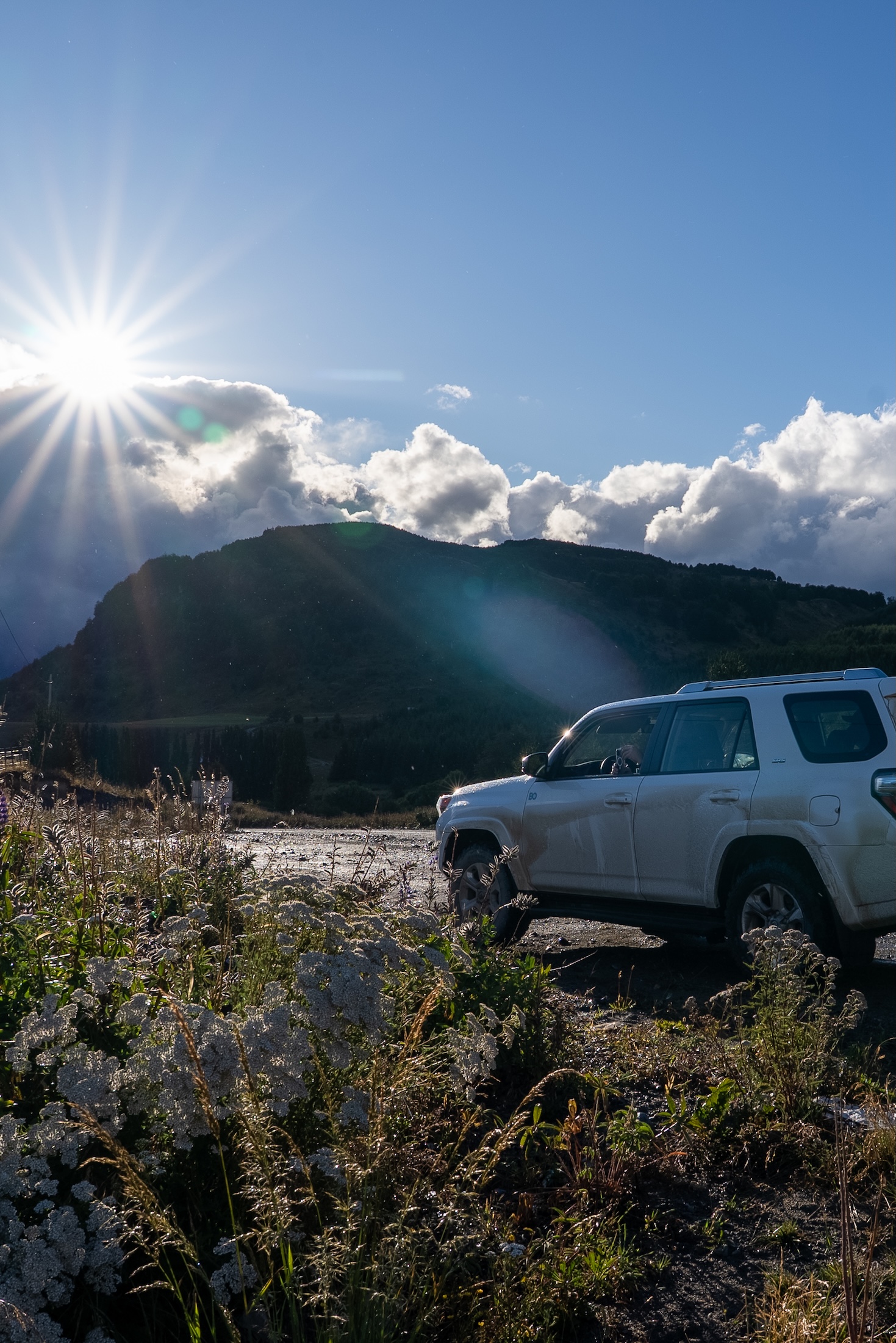 An SUV crosses the Patagonia landscape, with sun flaring over the mountains