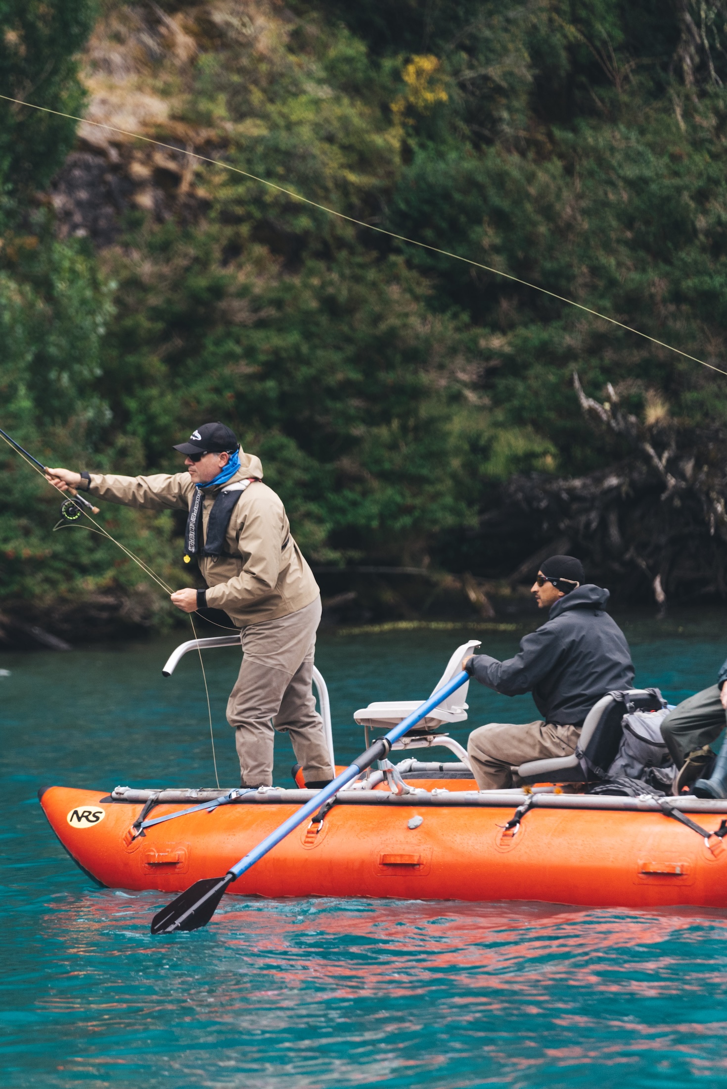 A man in an orange boat casts a fishing line while another person sits behind him