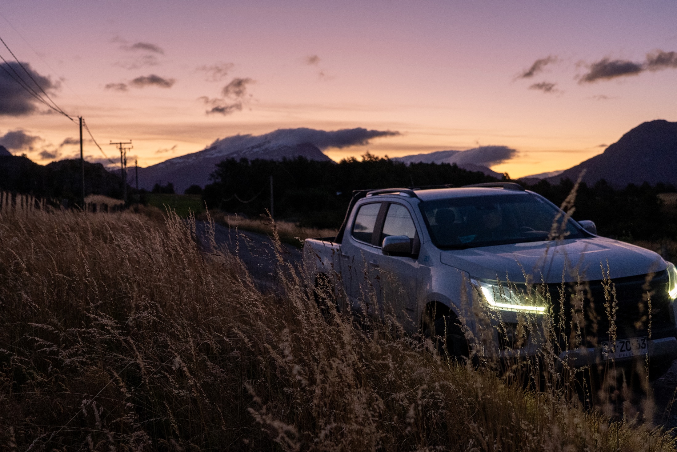 A pickup truck on a backroad, with a pink twilight sky in the background